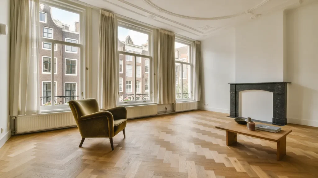 Woonkamer in een grachtenpand met licht eiken visgraat parket, hoge ramen en een fluwelen fauteuil